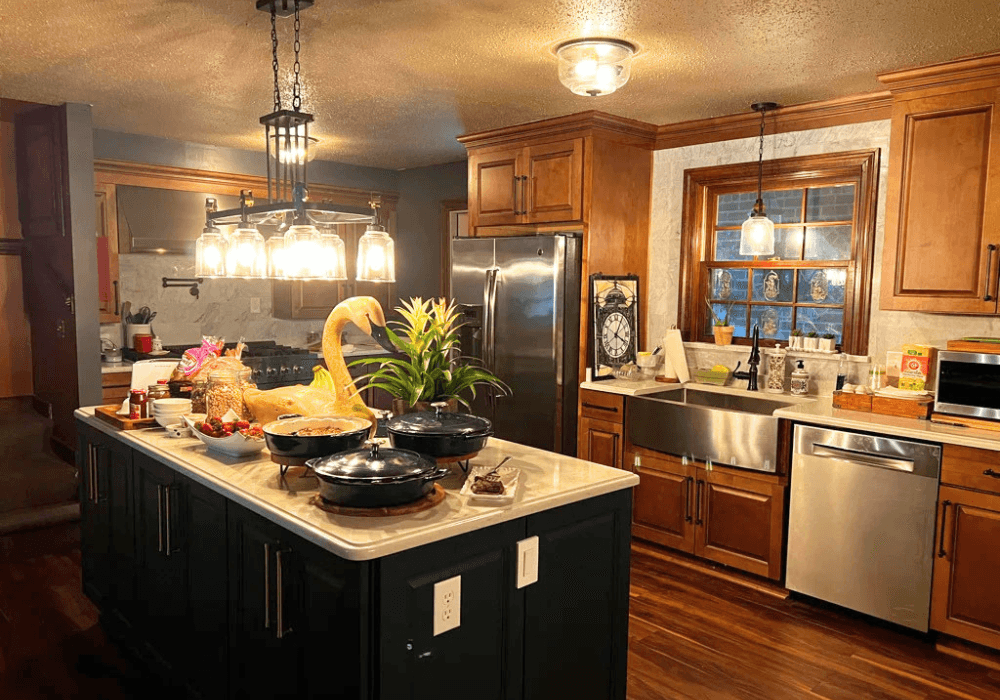 A warmly lit kitchen featuring wooden cabinets, an island with meal dishes, and a large window.