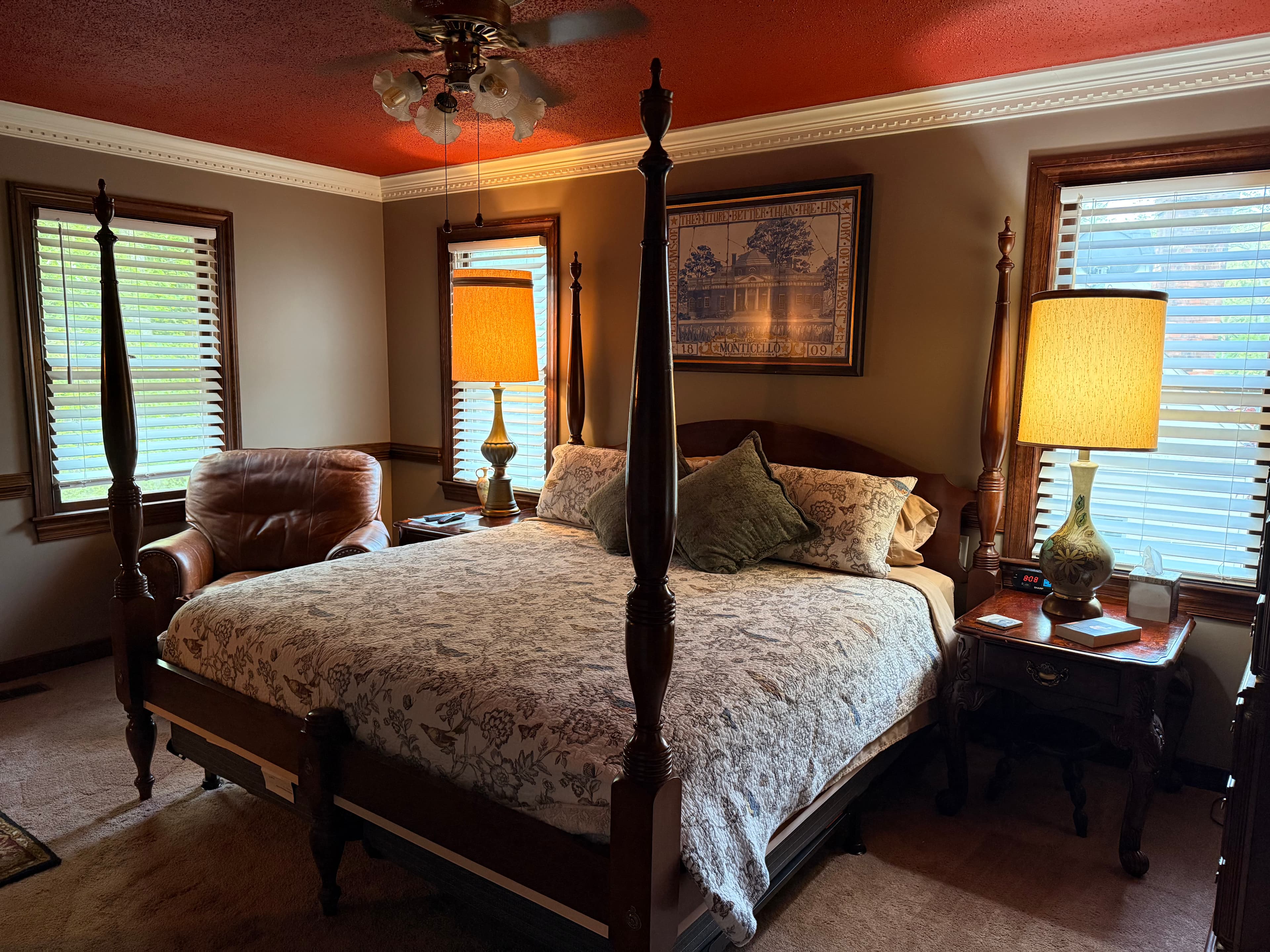 Cozy bedroom featuring a four-poster bed, armchair, and large windows with wooden blinds.
