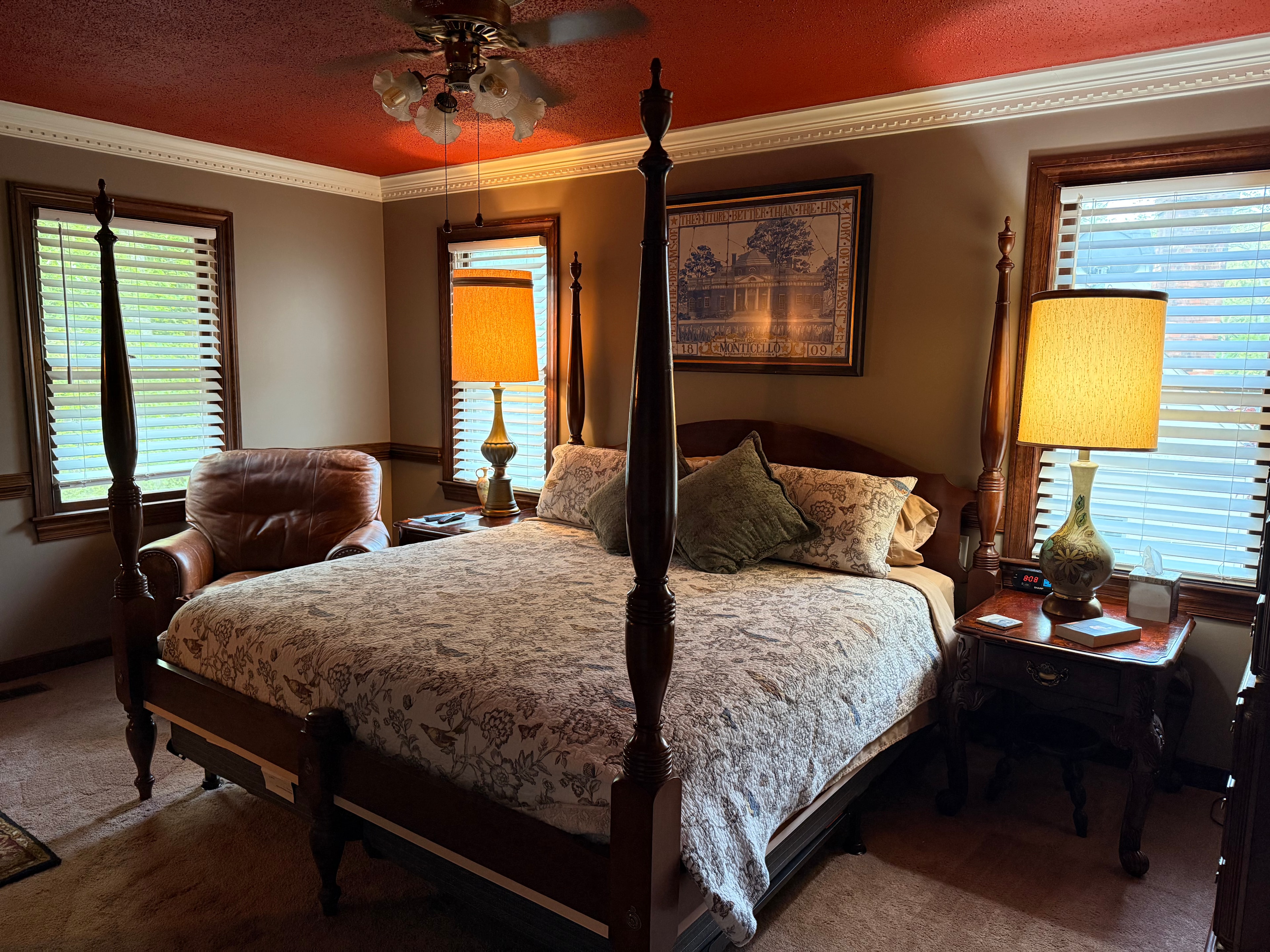 Cozy bedroom featuring a four-poster bed, armchair, and large windows with wooden blinds.