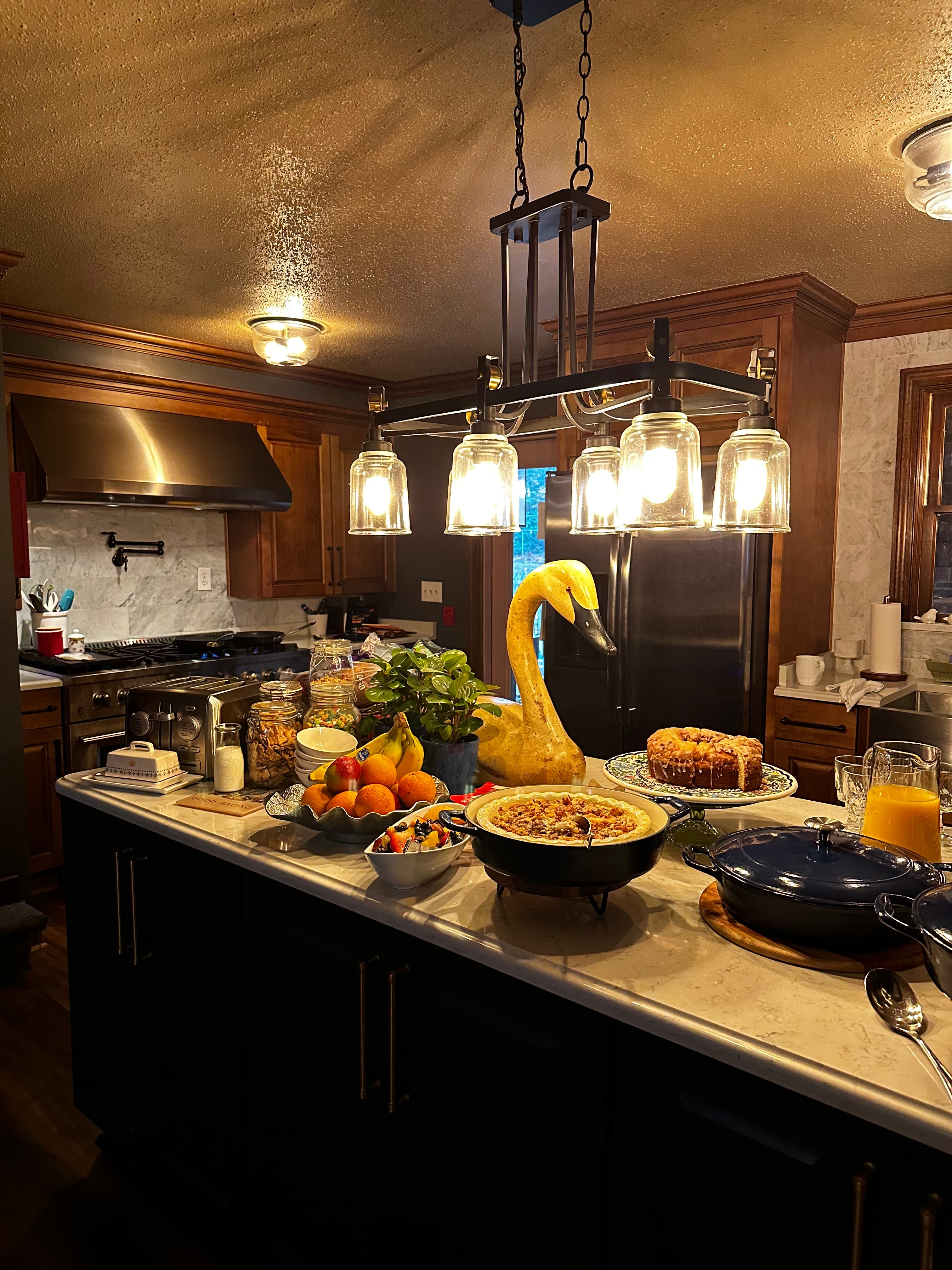 A elegantly arranged kitchen island with various dishes, fruits, and a decorative swan centerpiece under warm pendant lights.