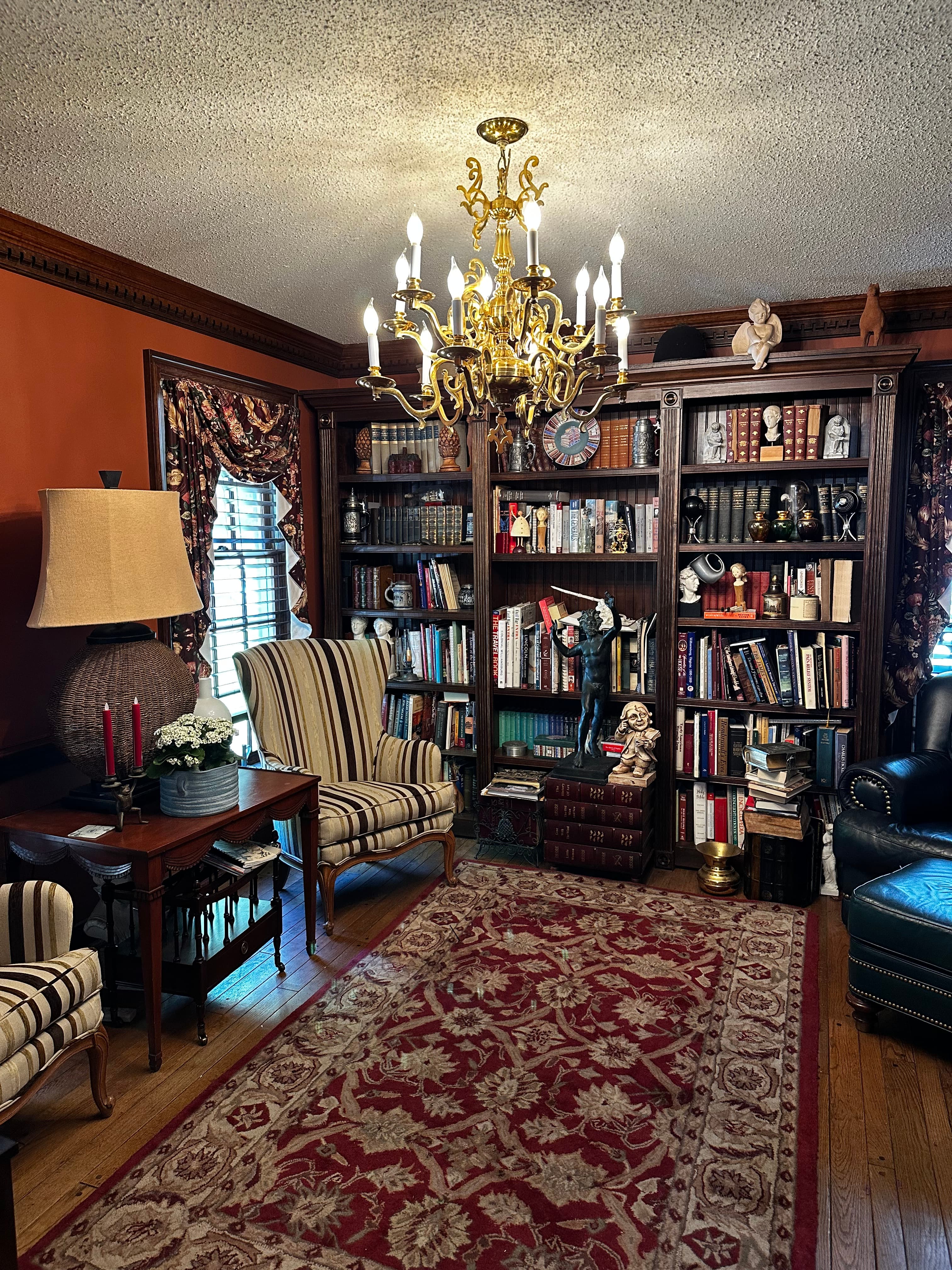 A cozy reading nook featuring striped chairs, a stylish chandelier, and a bookshelf filled with books.