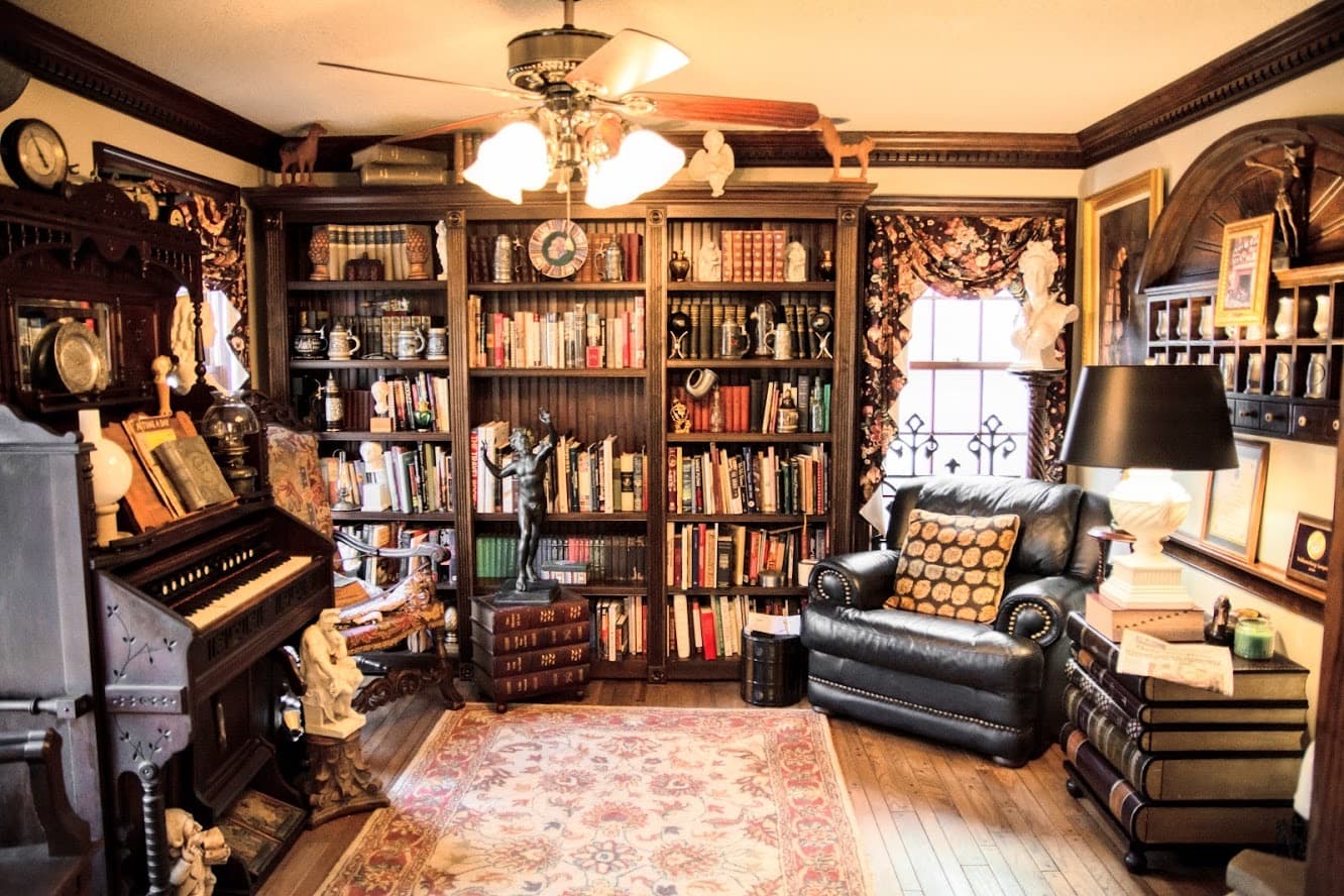 A cozy study featuring a large bookshelf filled with books, a piano, an armchair, and decorative accents.