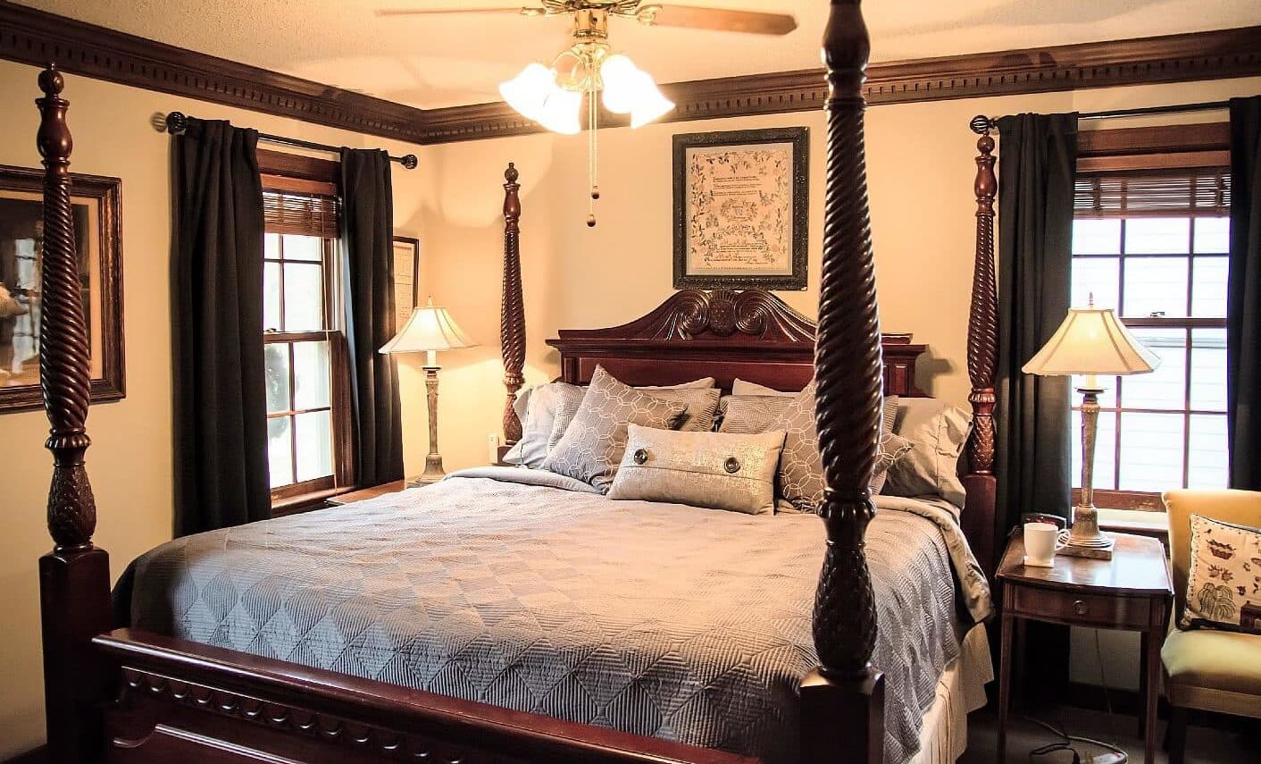 A warmly lit bedroom featuring a king-sized bed with decorative pillows, two bedside lamps, and wooden accents.