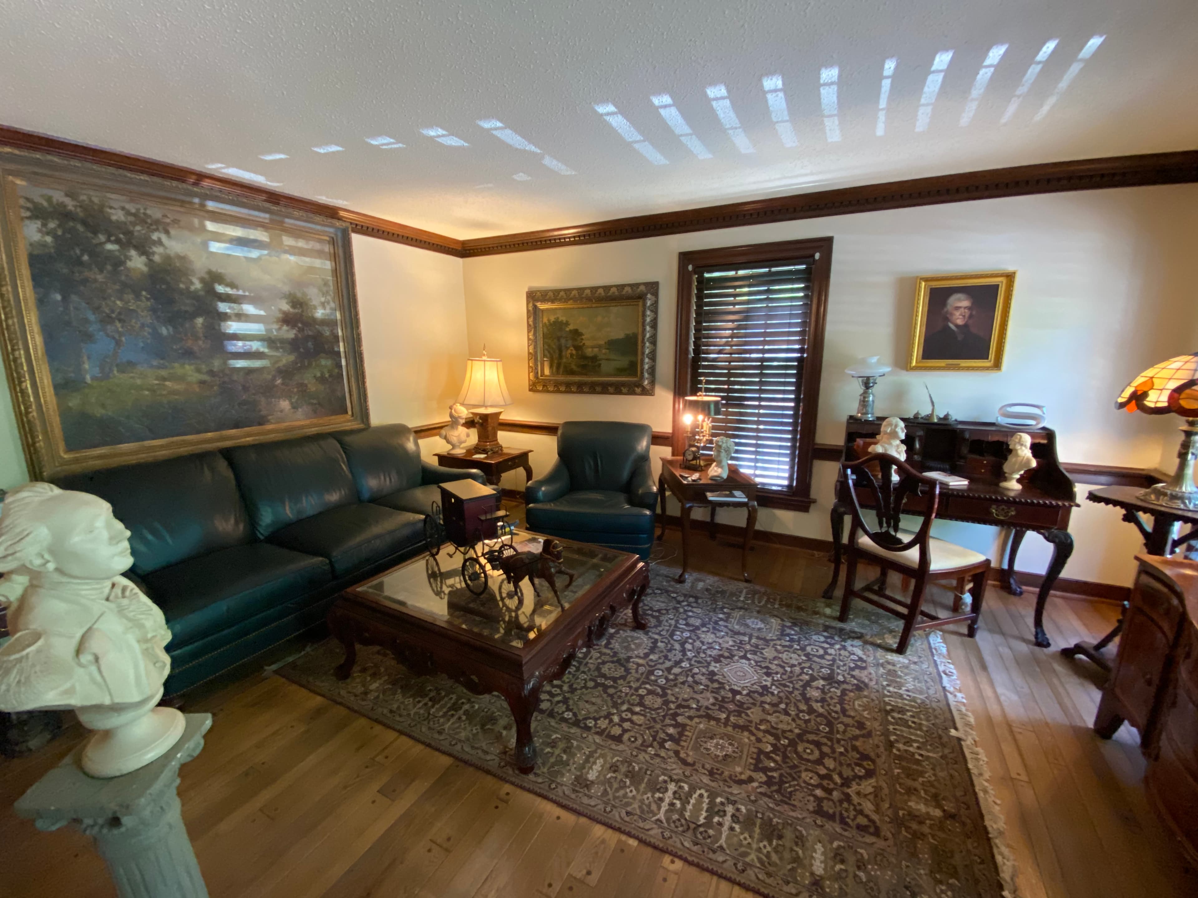 A cozy, vintage living room featuring a green leather sofa, ornate furniture, and classic artwork.