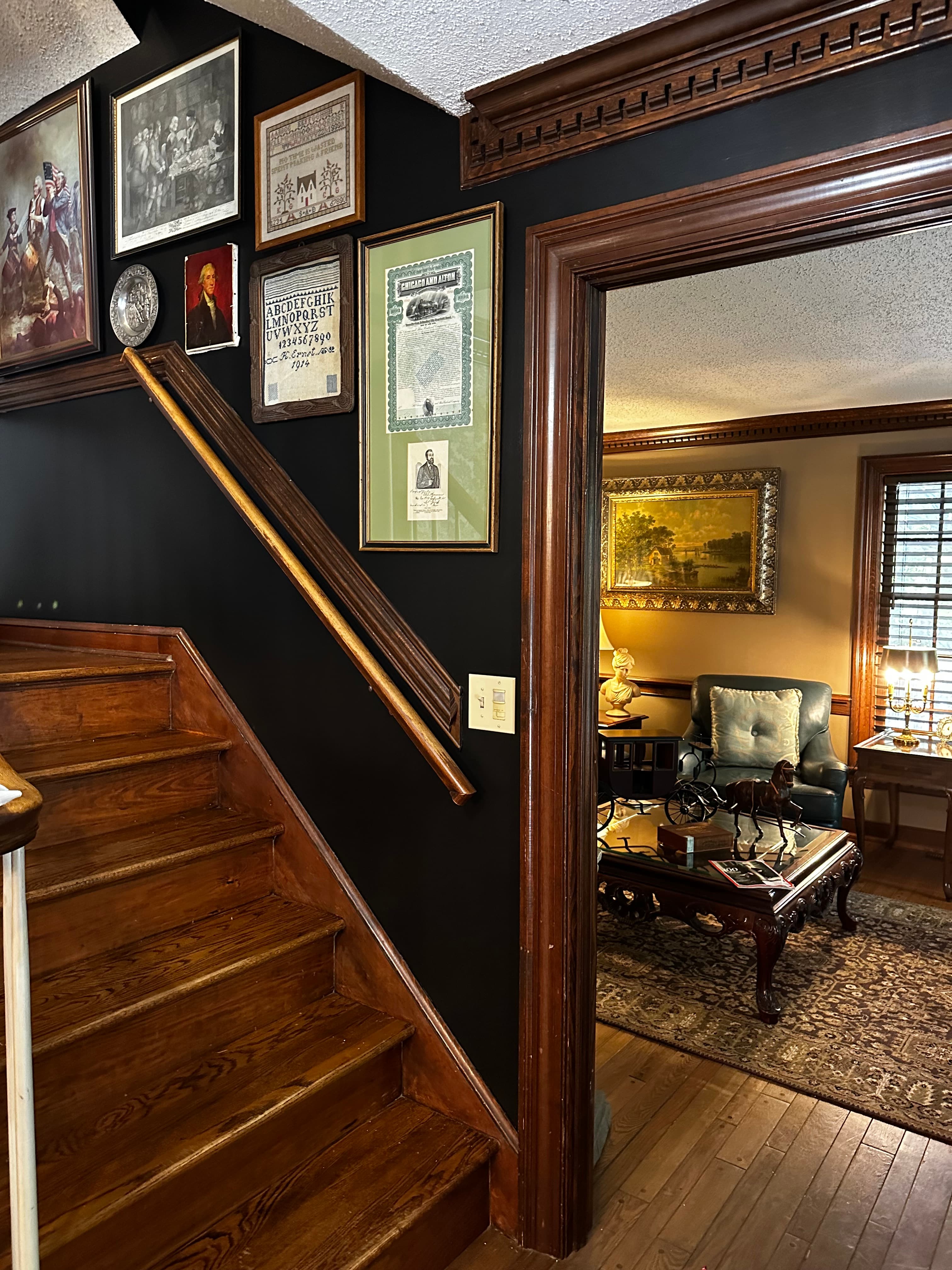 A wooden staircase leads to a hallway adorned with framed artwork, opening into a cozy living room.